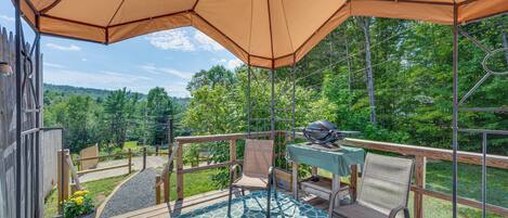 A covered outdoor deck with a barbecue grill, seating, and a view of the surrounding greenery.