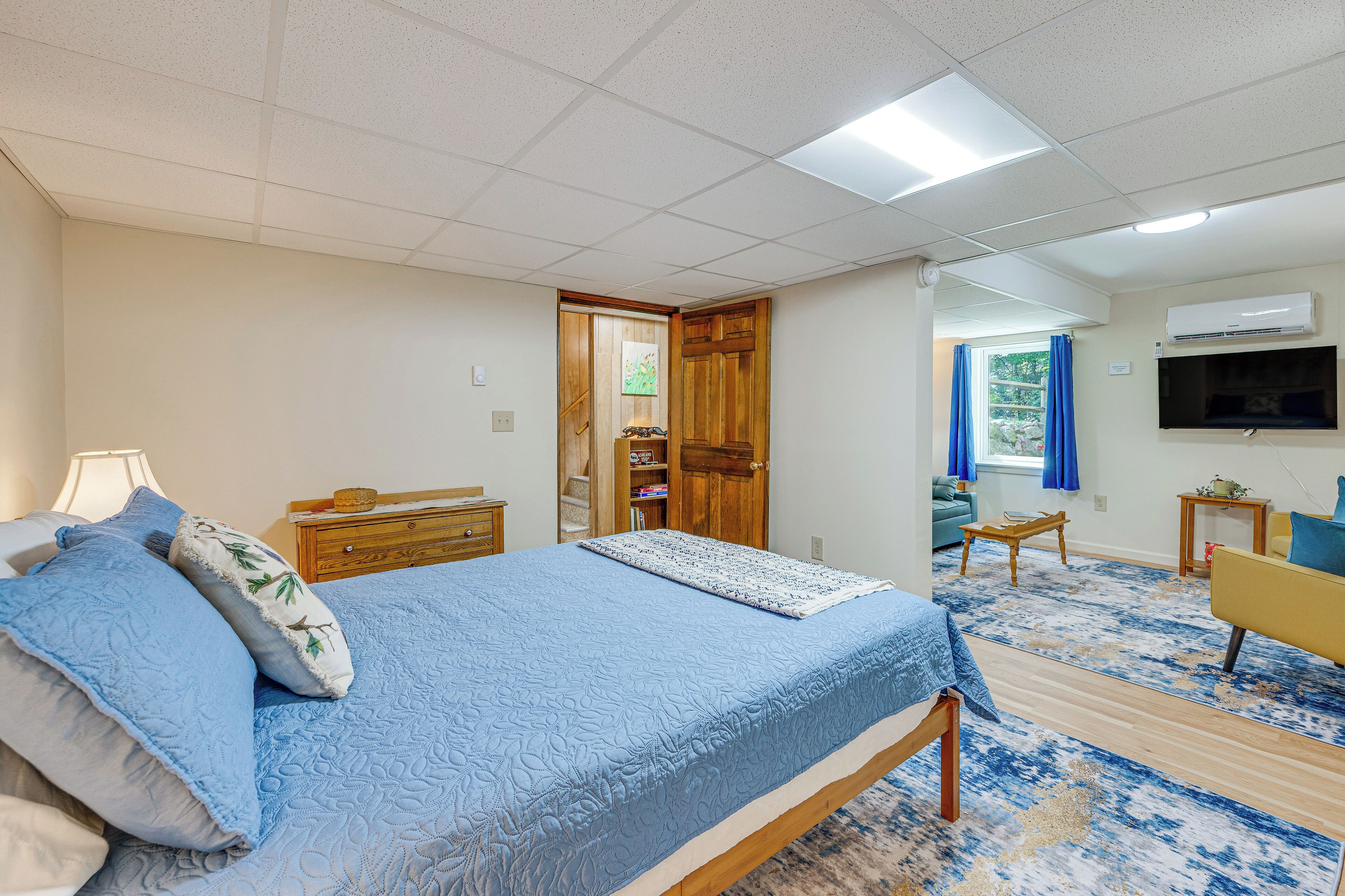 A bedroom with a bed, bedside table, lamp, dresser, and a television.