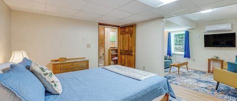 A bedroom with a bed, bedside table, lamp, dresser, and a television.