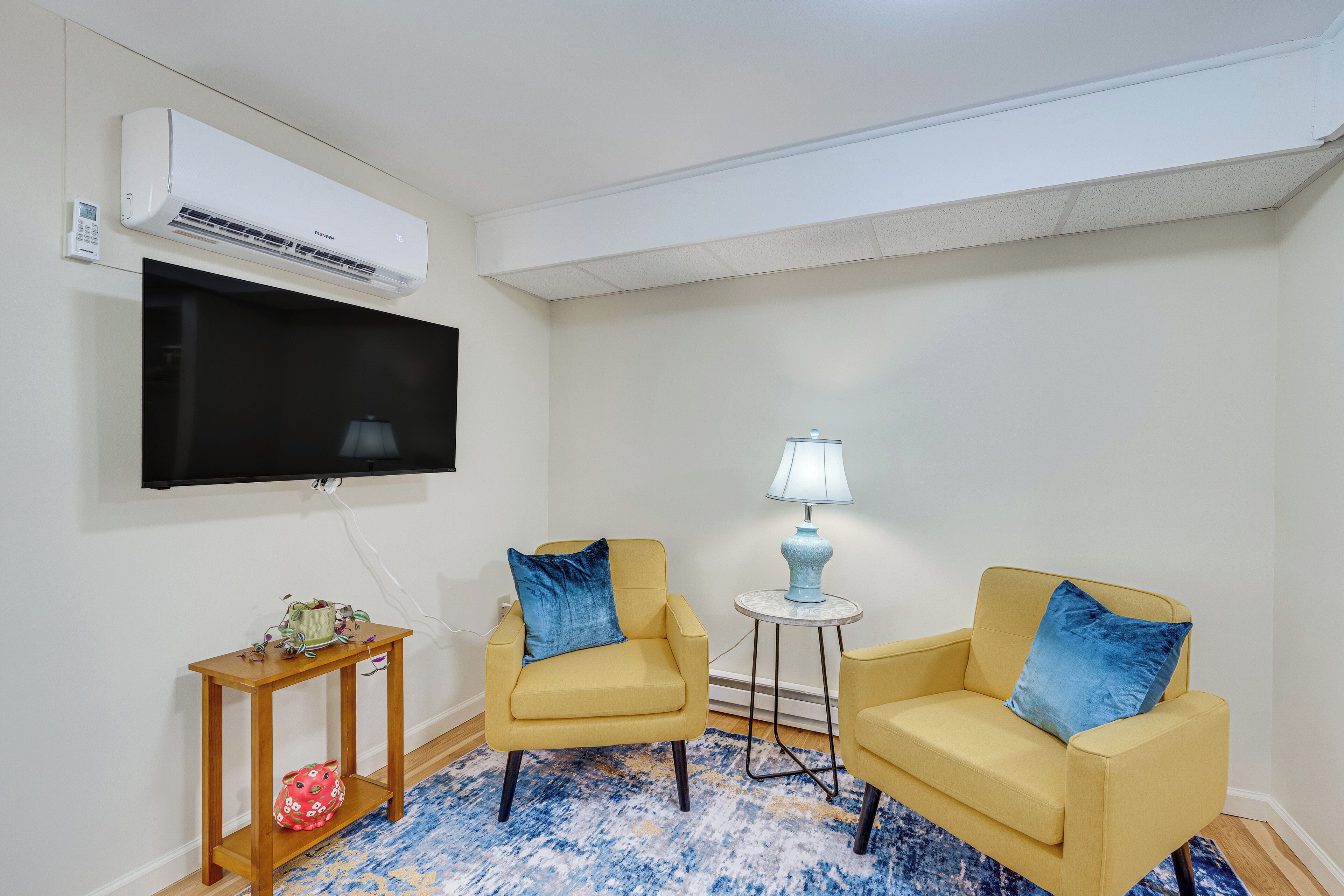 A living room with two yellow armchairs, a small side table, a lamp, a television, and a wall-mounted air conditioner.