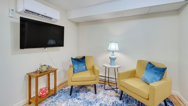 A living room with two yellow armchairs, a small side table, a lamp, a television, and a wall-mounted air conditioner.
