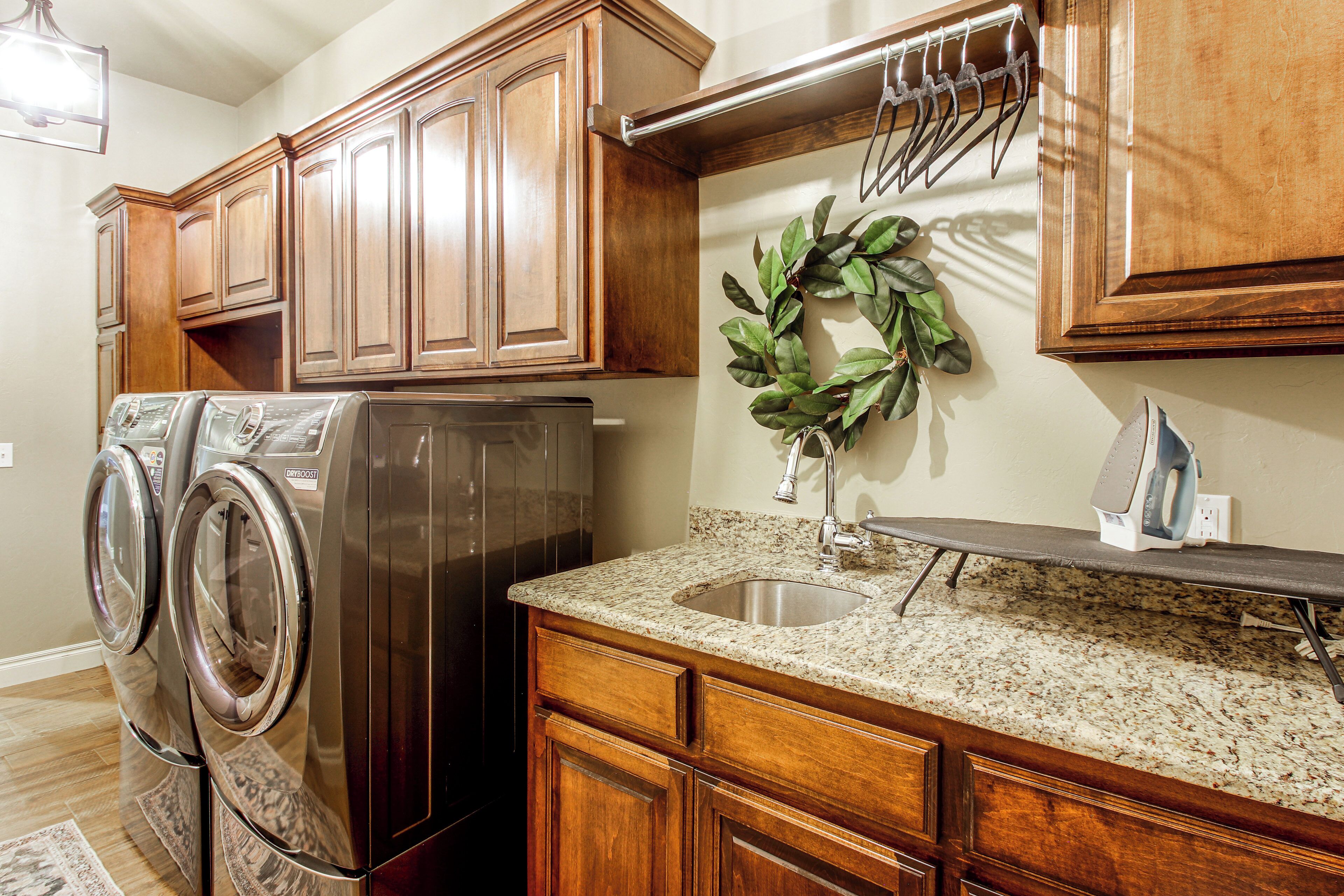 A kitchen with wooden cabinets, a stainless steel refrigerator, a granite countertop, a sink, and a wall-mounted drying rack.