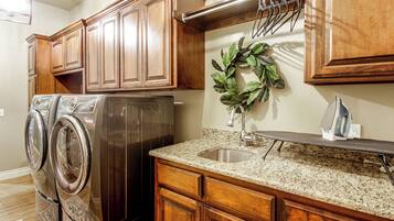 A kitchen with wooden cabinets, a stainless steel refrigerator, a granite countertop, a sink, and a wall-mounted drying rack.