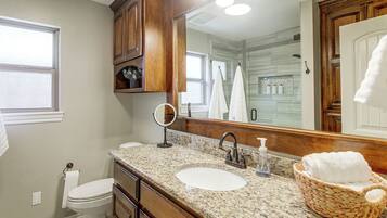 Un baño con encimera de granito, un lavabo blanco, un espejo y un mueble de madera.