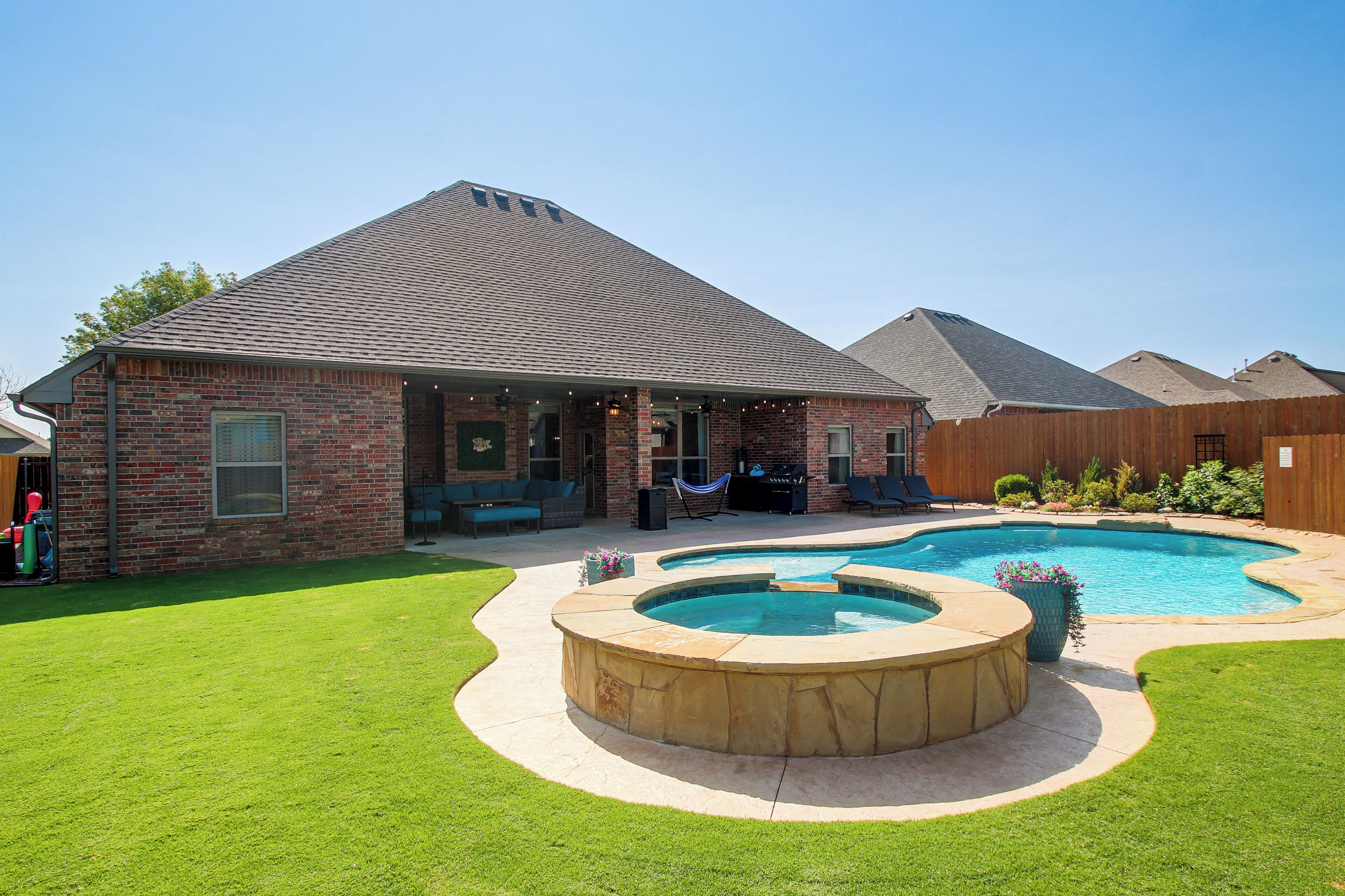 Una propiedad residencial con una casa de ladrillo, piscina y jardín ajardinado.
