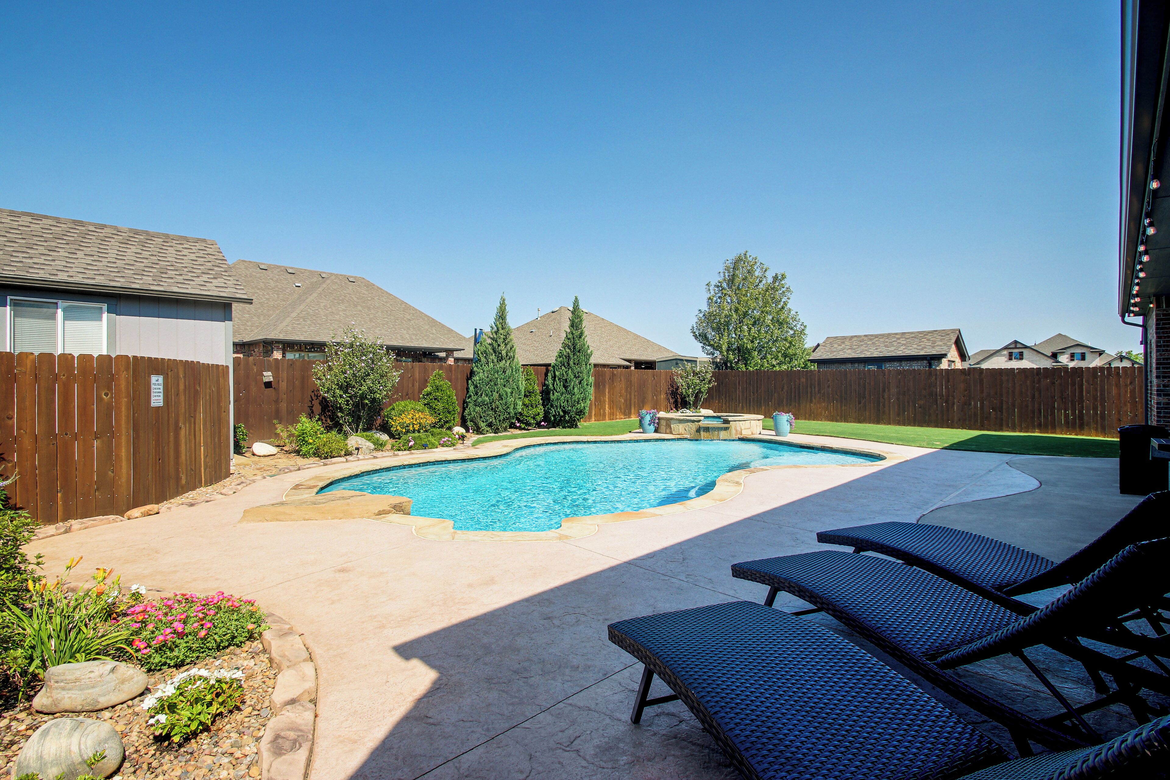 Un jardin avec une piscine, une clôture en bois et un espace patio aménagé avec des chaises longues.
