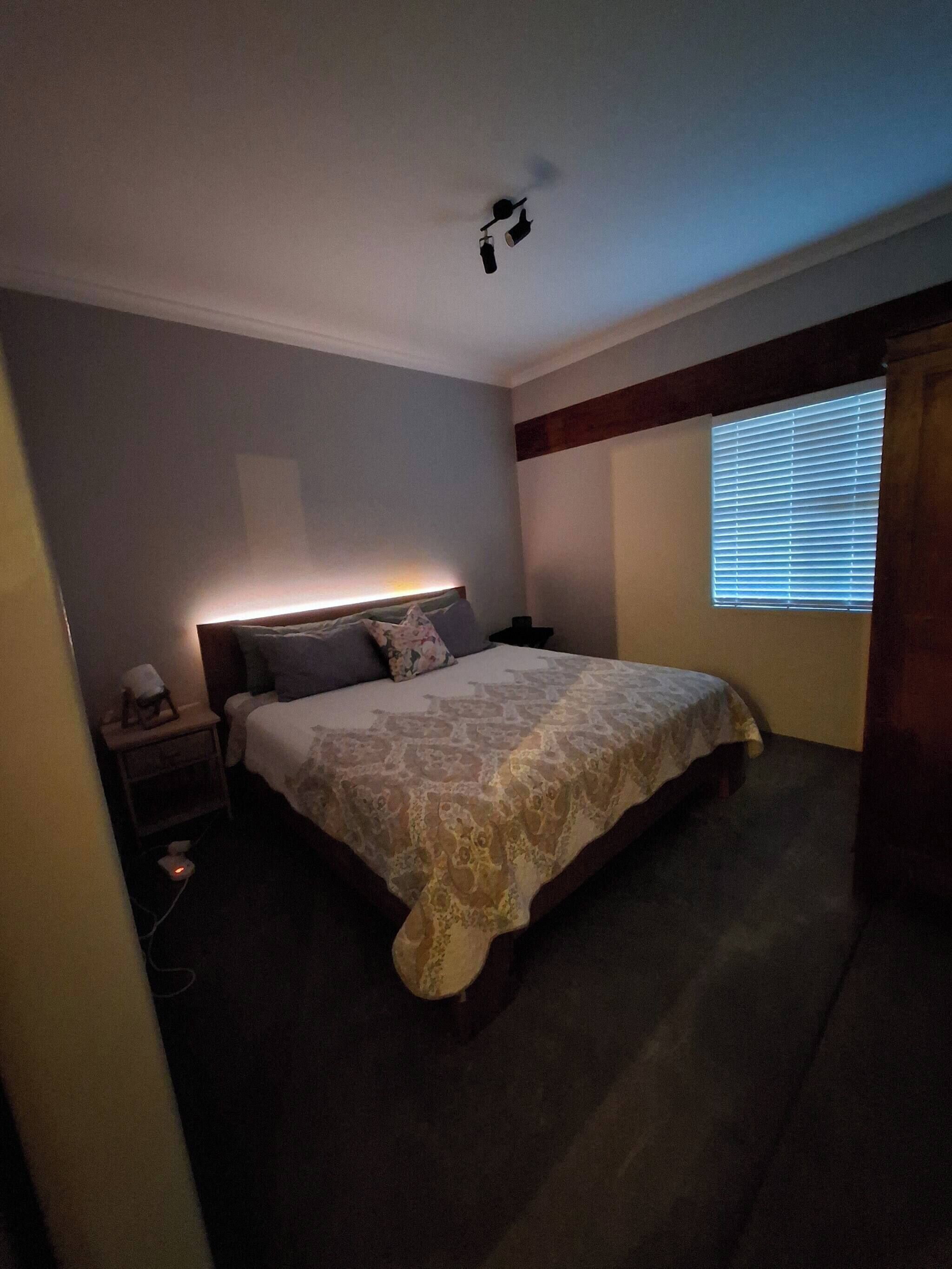 A bedroom with a bed, bedside table, and a window with blinds.