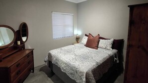 A bedroom with a bed, dresser, mirror, window, and ceiling light.