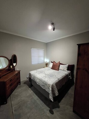 A bedroom with a bed, dresser, mirror, window, and ceiling light.