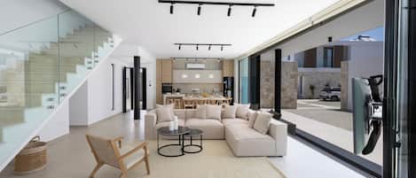 A modern interior with a sectional sofa, a wooden chair, a small table, and a staircase with glass railings.