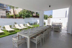 An outdoor dining area with a long table and multiple chairs, a pool, and a covered seating area with lounge chairs. - New, 4 bedroom villa with pool, 100 meters from the beach (Paralimni)