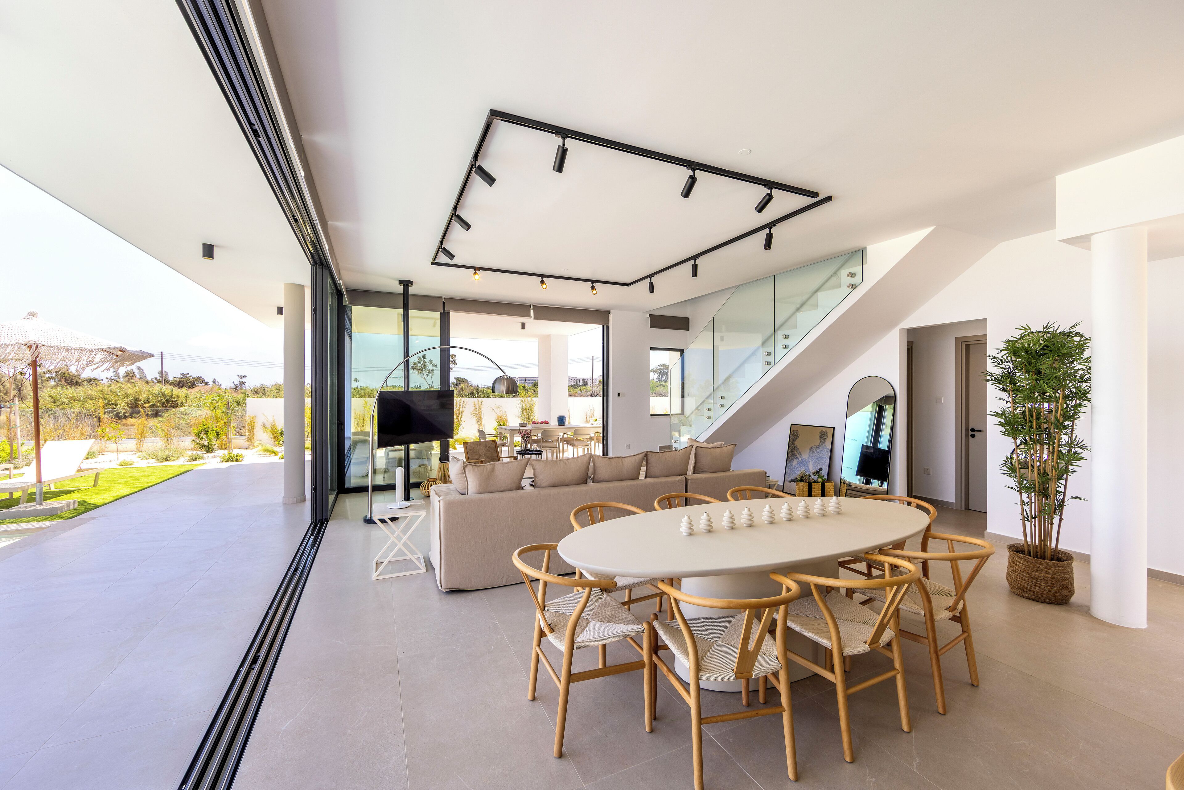 A modern living room with a large sofa, a dining table with chairs, a TV, and a staircase leading to an upper level.