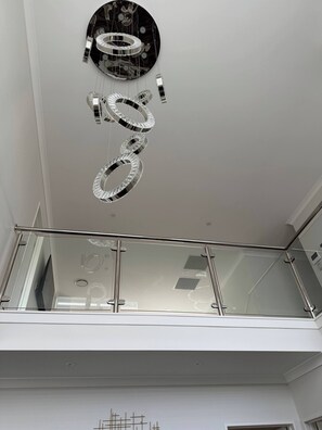 A modern interior with a reflective ceiling fixture and a glass railing.