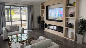 A modern living room with a flat-screen TV, comfortable seating, and a view of the outdoors.