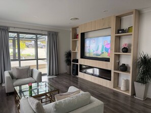A modern living room with a flat-screen TV, comfortable seating, and a view of the outdoors.