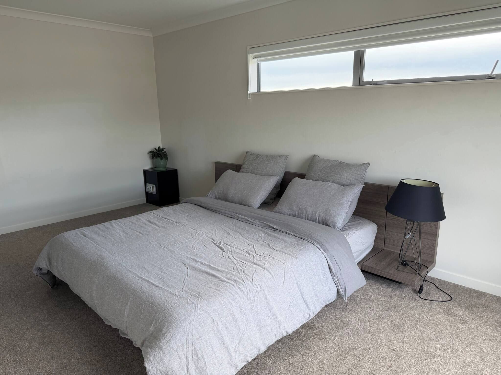 A bedroom with a bed, a bedside table, a lamp, and a window.