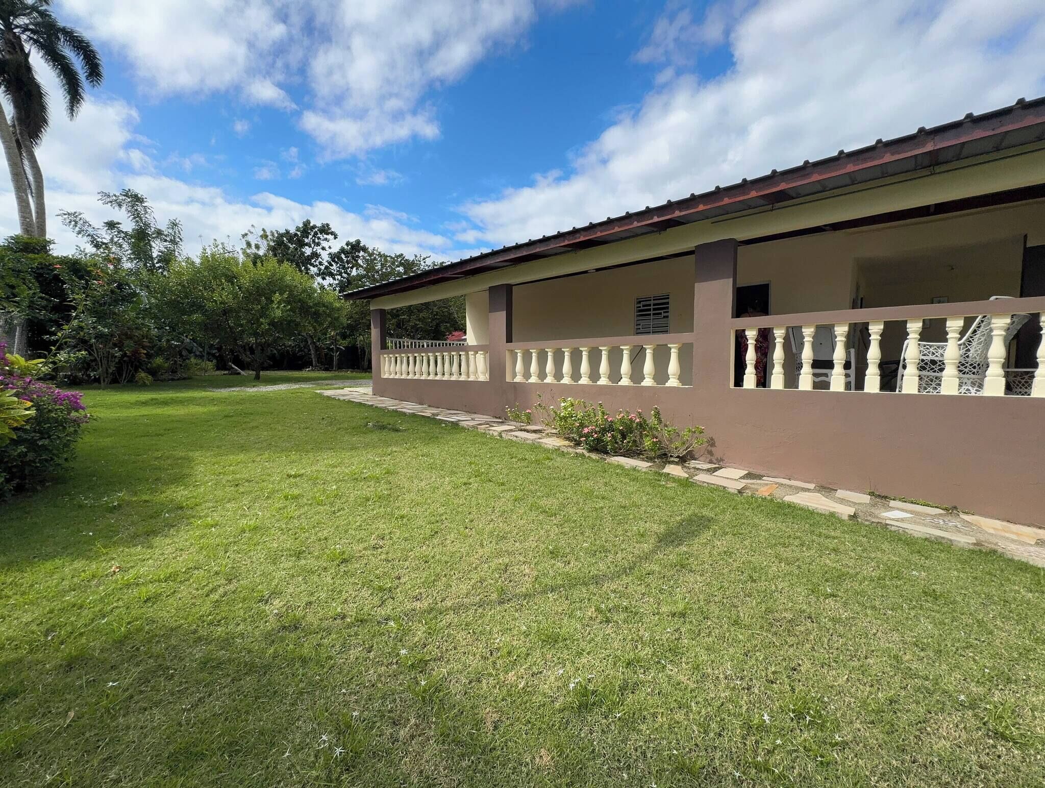 A residential building with a covered patio area, a well-maintained lawn, and surrounding greenery.