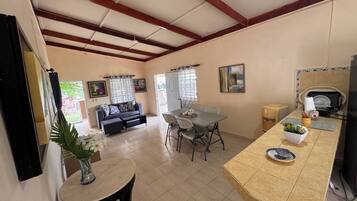 A spacious living area with a dining table, sofa, and kitchen area with a refrigerator and sink.