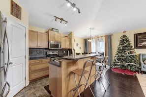 A kitchen with wooden cabinets, a built-in oven, and a bar area with stools. - Shalom Casablanca Home (Edmonton)