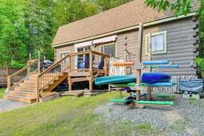 A wooden cabin with a staircase leading to a deck, surrounded by trees.