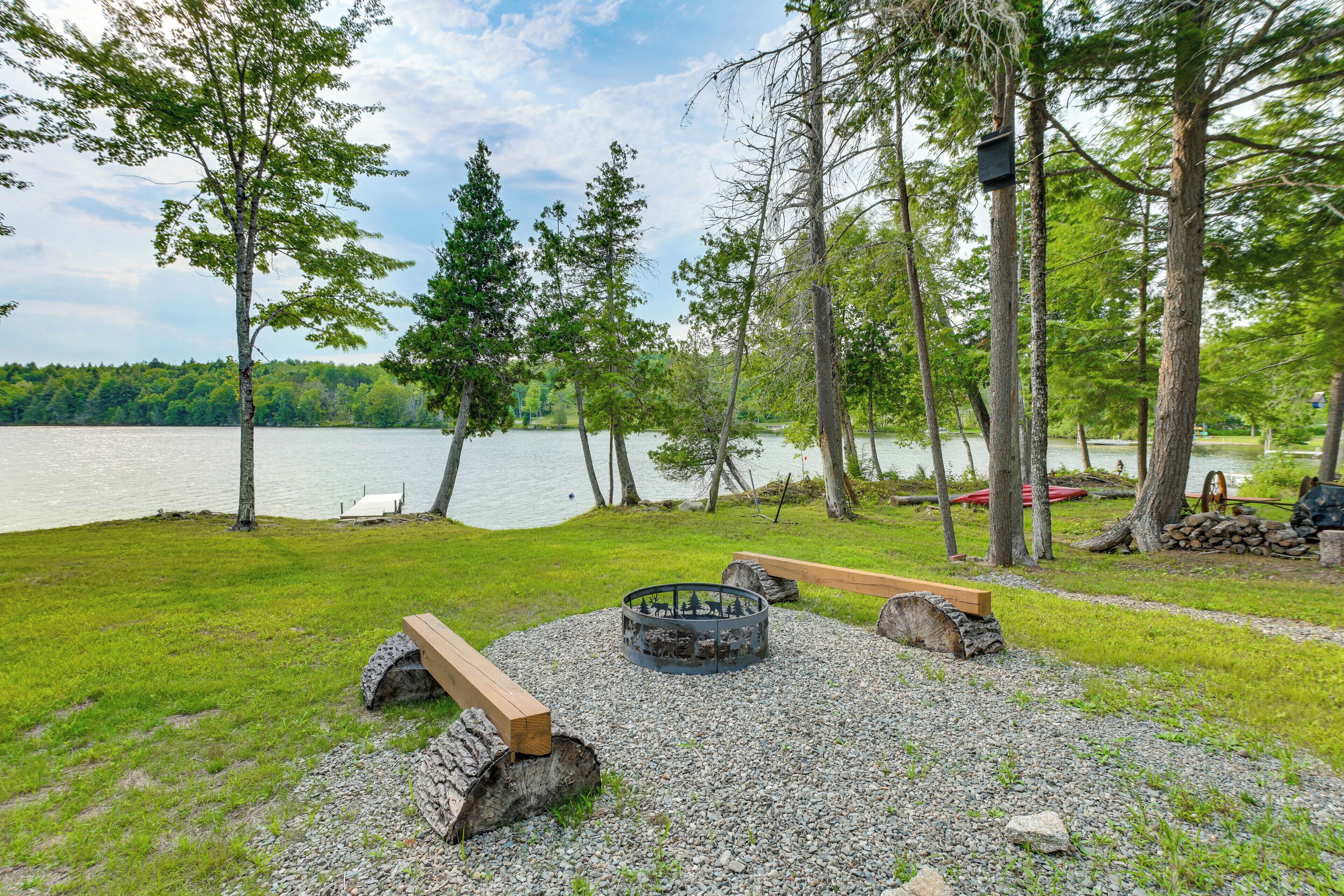 A lakeside outdoor seating area with a fire pit, benches, and a dock.