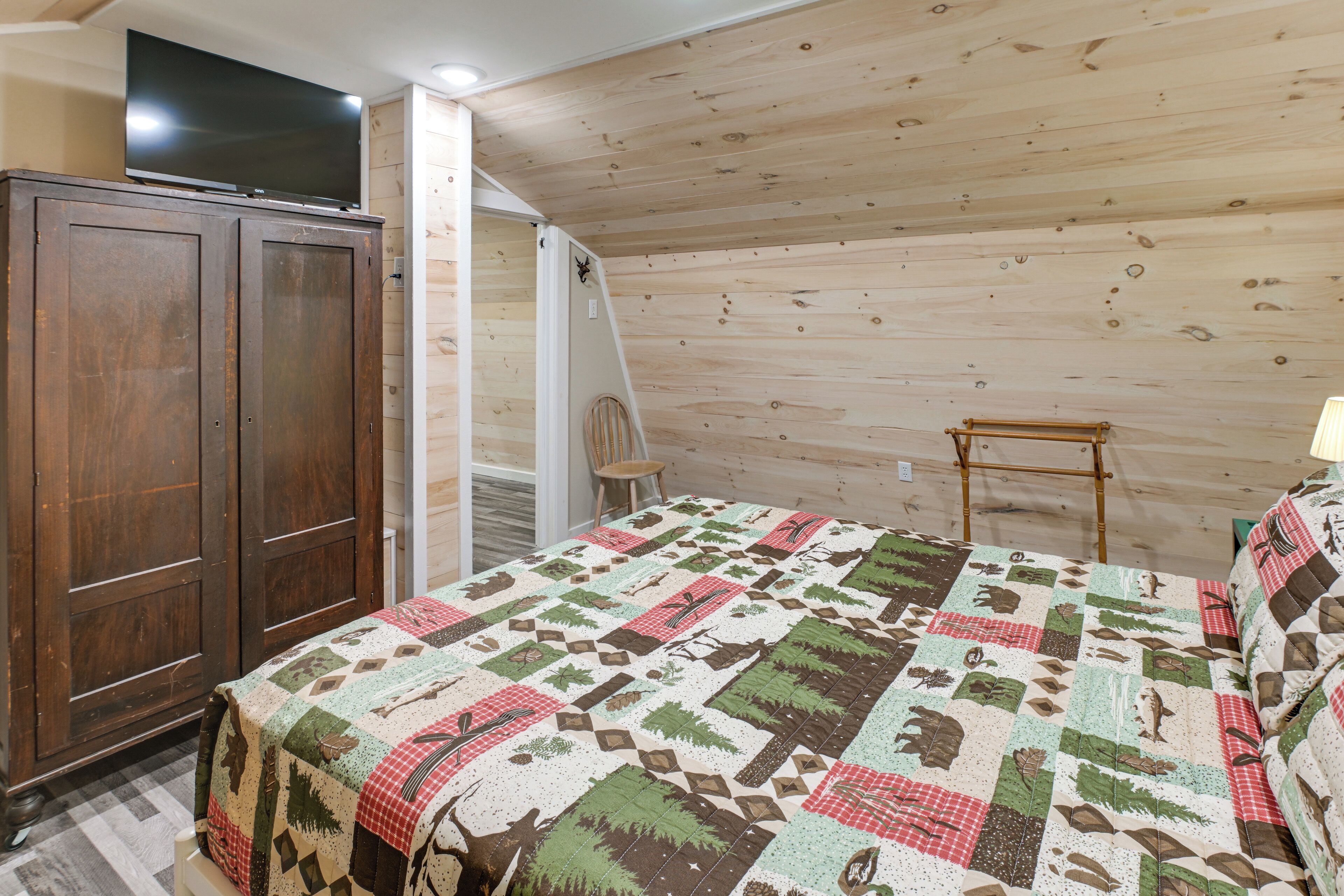 Une chambre avec un plafond en bois, un lit recouvert d’une courtepointe à motifs, une armoire en bois et une chaise.