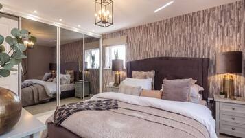 A bedroom with a large mirror, a bed with multiple pillows, bedside tables with lamps, and a ceiling light fixture.