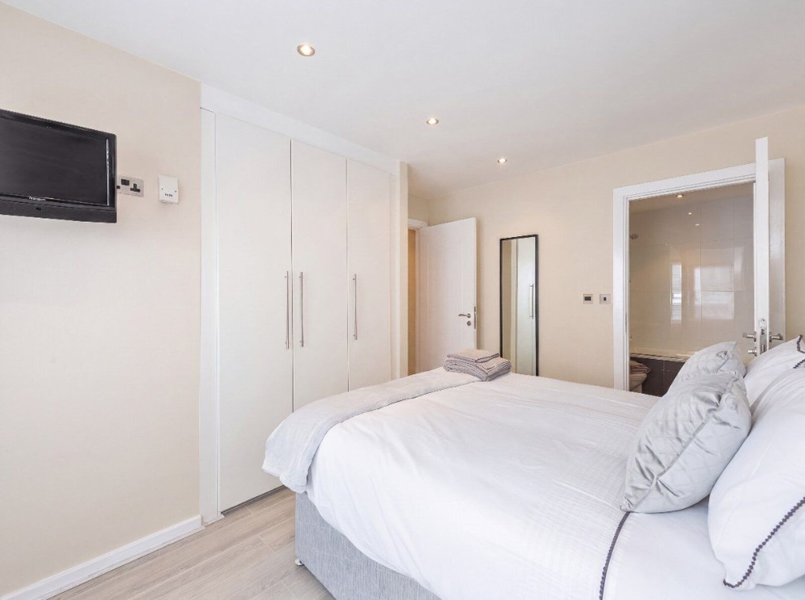 A bedroom with a bed, a wardrobe, a mirror, and a television on the wall.