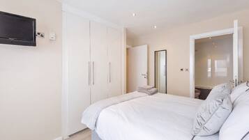 A bedroom with a bed, a wardrobe, a mirror, and a television on the wall.