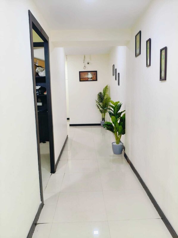 A hallway with a door leading to a room, a potted plant, and framed pictures on the wall.
