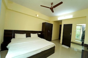 A hotel room with a bed, wardrobe, ceiling fan, and a door leading to another room.