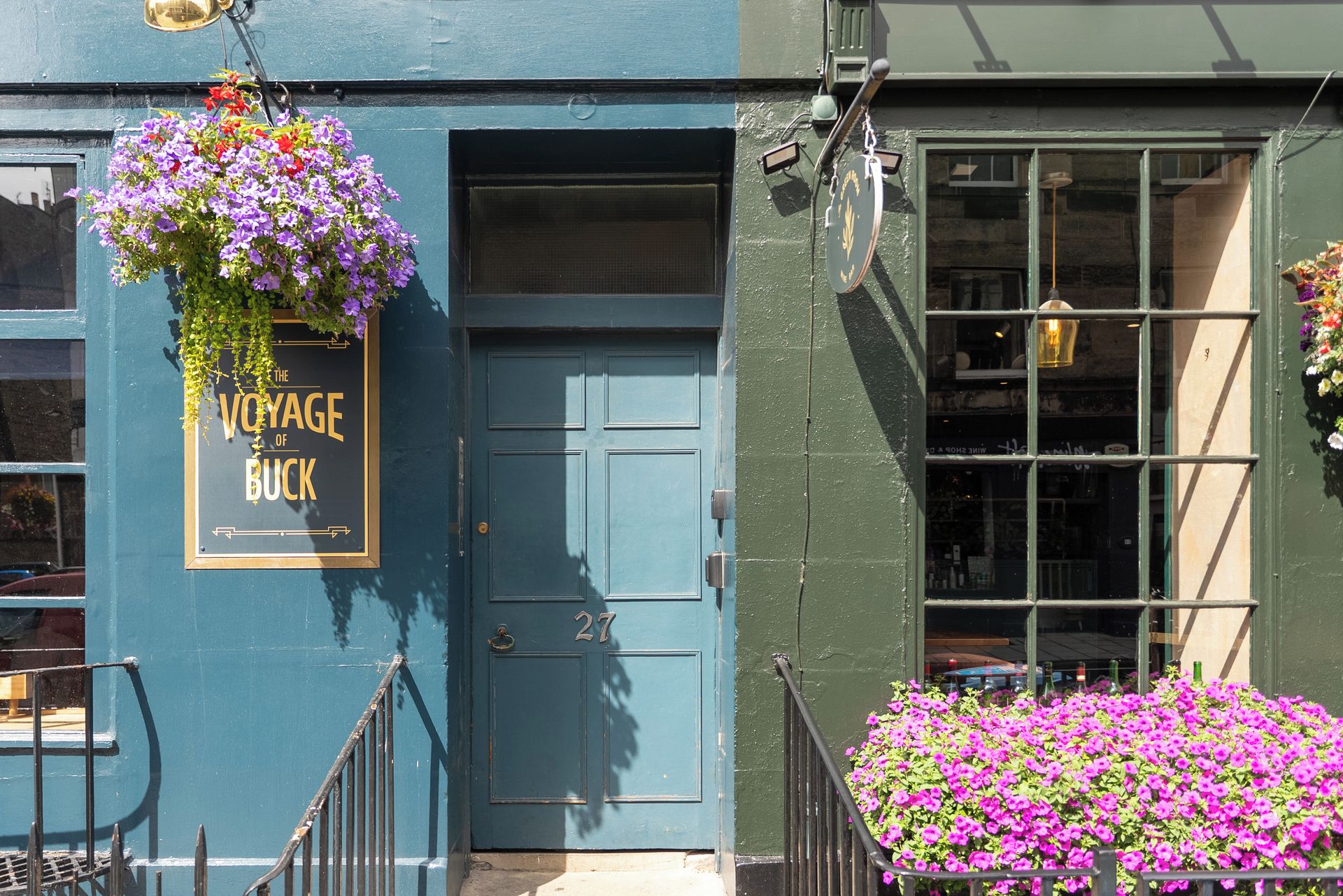Un immeuble avec une porte bleue portant le numéro 27, une jardinière suspendue et une fenêtre donnant sur la rue.