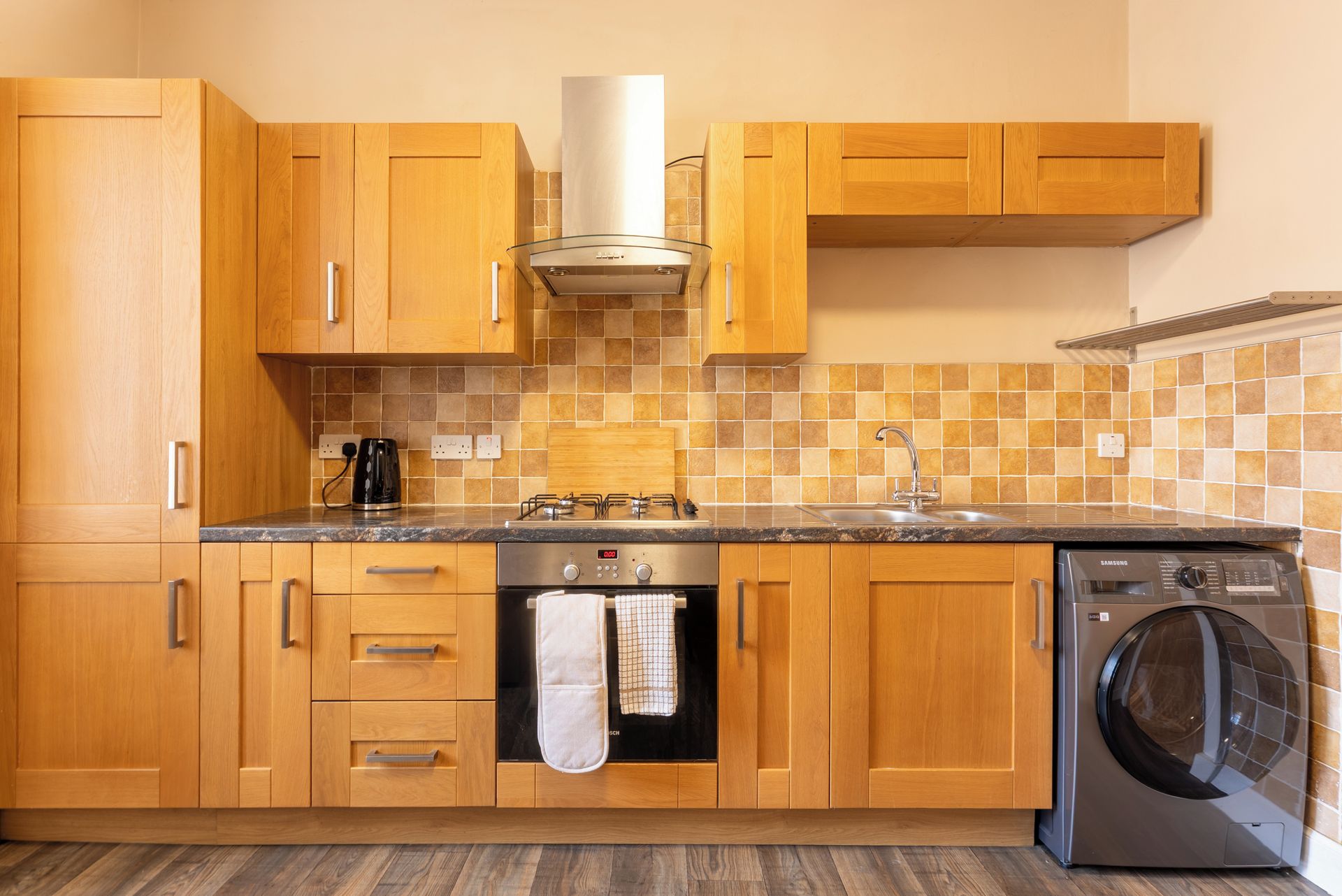 A modern kitchen with wooden cabinets, a stainless steel range hood, a built-in dishwasher, and a tiled backsplash.