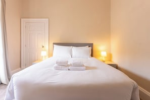 A neatly made bed with white linens and towels, two bedside lamps, and a closed door in a hotel room.