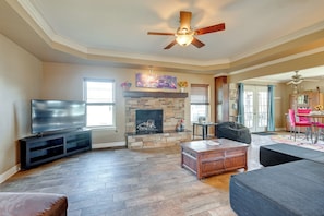 A living room with a stone fireplace, a ceiling fan, a flat-screen TV, and a dining area with a table and chairs. - Swim, Grill & Relax! Copperas Cove Family Home (Copperas Cove)