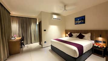 A hotel room with a large bed, a desk, a chair, a ceiling fan, and a painting on the wall.