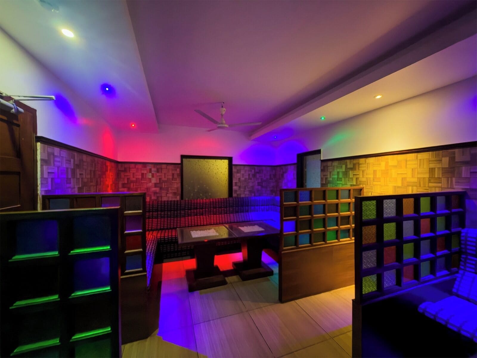 A room with a ceiling fan, a seating area with a table, and a wall with a textured pattern.