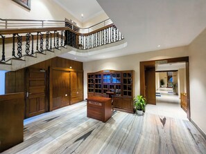 Un vestíbulo de hotel con suelo de mármol, un mostrador de recepción de madera, una escalera con barandilla ornamentada y una estantería.