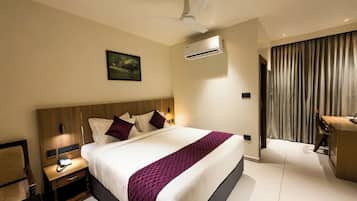 A hotel room with a bed, bedside table, nightstand, and an air conditioning unit.