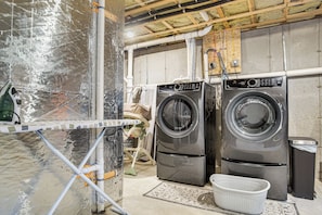 A laundry room with two front-loading washing machines, a drying rack, and a trash bin. - Beautiful West Harwich Home: 1 Mile to Beach! (Harwich)