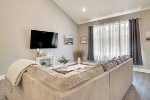 A living room with a large sectional sofa, a flat-screen TV, a coffee table, and a window with curtains. - Beautiful West Harwich Home: 1 Mile to Beach! (Harwich)