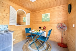 A wooden cabin with a dining area, a kitchen, and a fan.