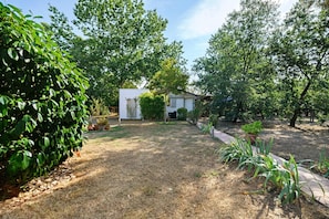 A residential backyard with a small white shed, a lawn, and various plants. - Bed and Breakfast 'Chambre D'hôtes Les Coquelicots' with Private Terrace, Wi-Fi and Air Conditioning (Fronton)