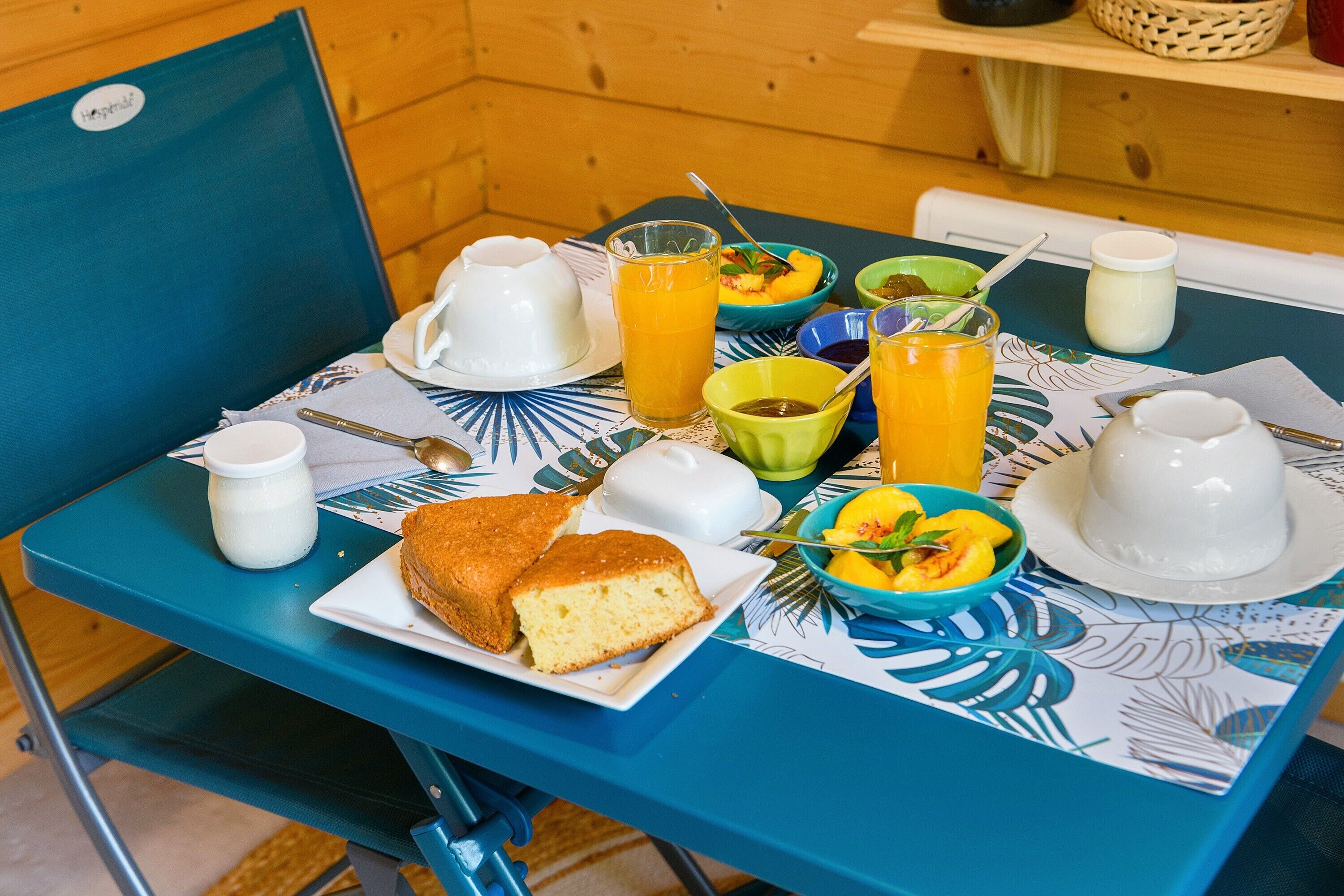 Une table de petit-déjeuner avec une assiette de nourriture, un verre de jus d’orange, ainsi que divers bols et tasses.