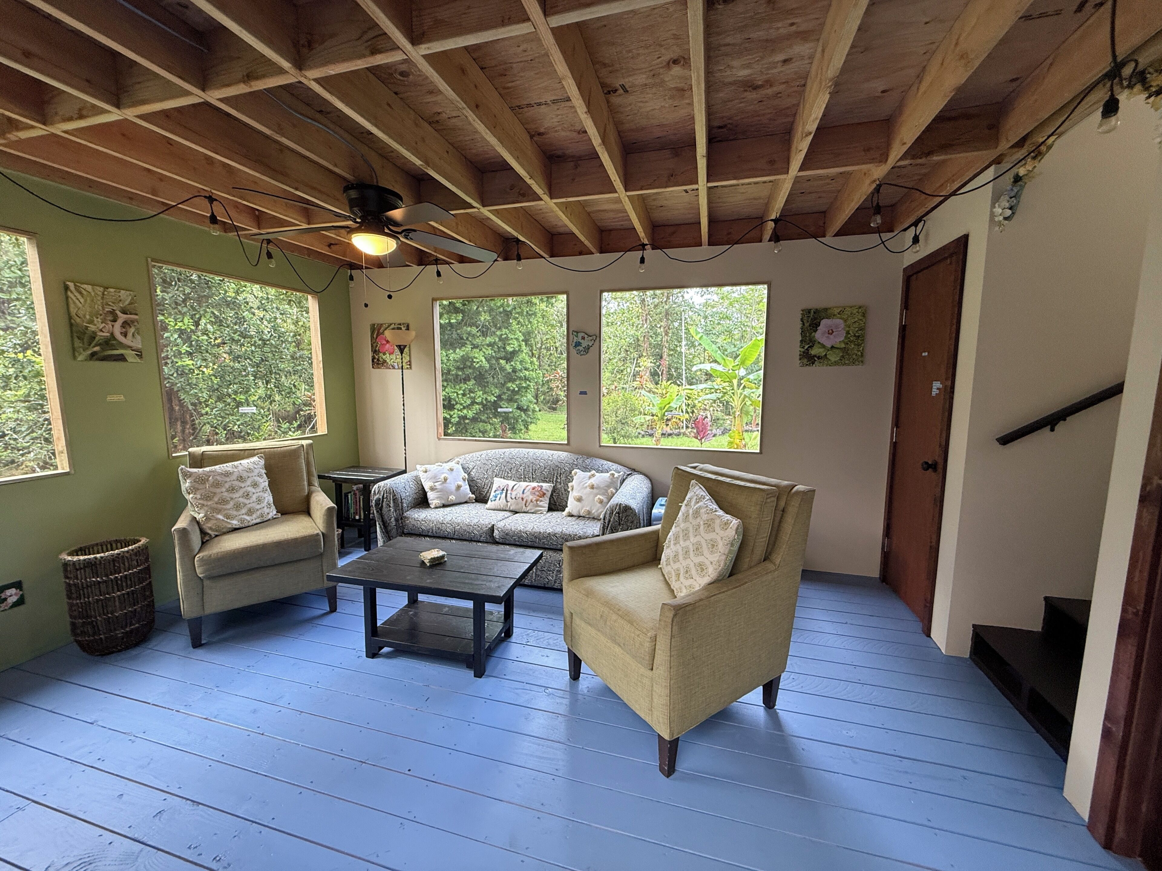 A cozy room with a wooden ceiling, a sofa set, a coffee table, and large windows offering a view of greenery.