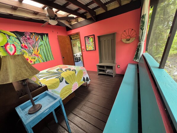 A room with a bed, a ceiling fan, a wooden bench, and a colorful wall mural.