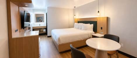 A hotel room with a bed, a desk, a chair, and a round table.