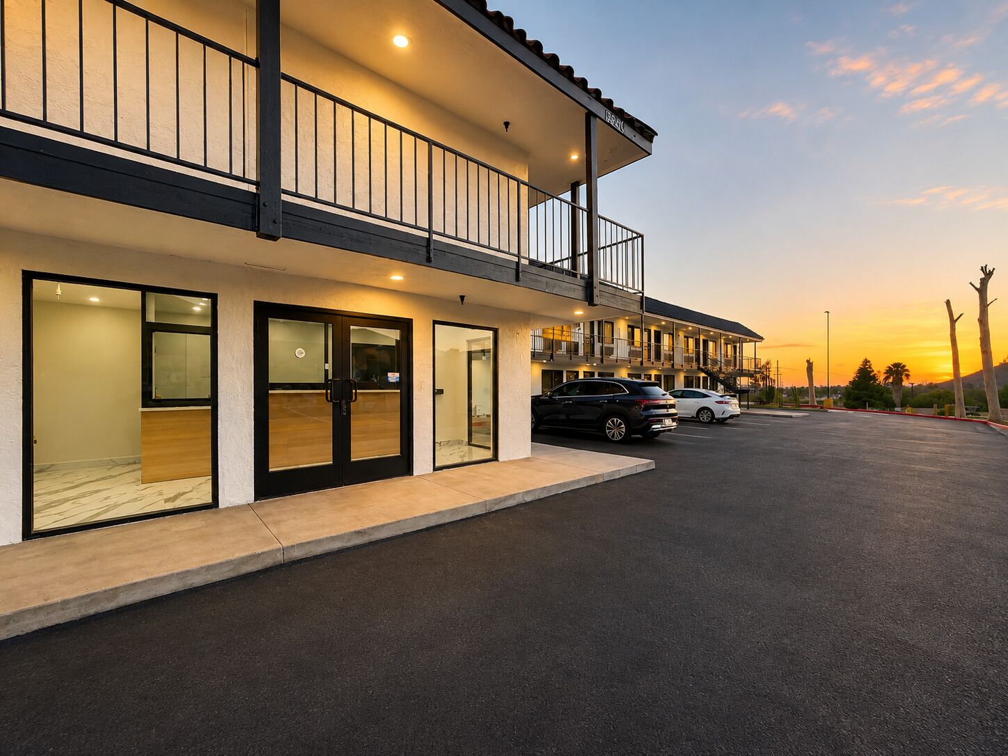 A hotel with a two-story structure, a covered parking area, and a sunset in the background.