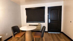 A small room with a round table, two chairs, a heater, a window with a blind, and a door.