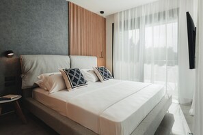 A modern bedroom with a large bed, a bedside table, and a view of the outdoors through sheer curtains.